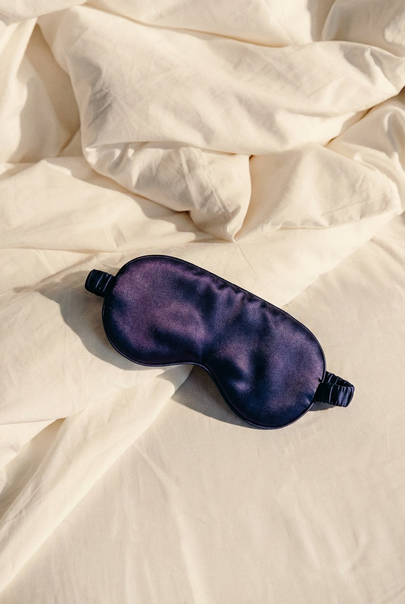 Navy silk sleep mask on white linen bedding, representing deep restful sleep supported by MagZorb Sleep