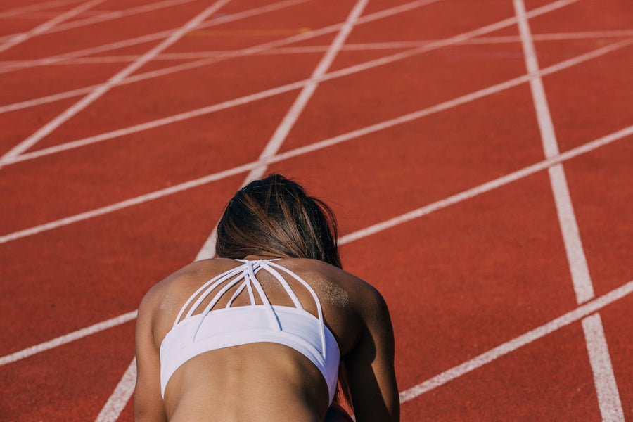 Woman resting head-down on a red running track, representing iron deficiency fatigue and the need for effective iron support.